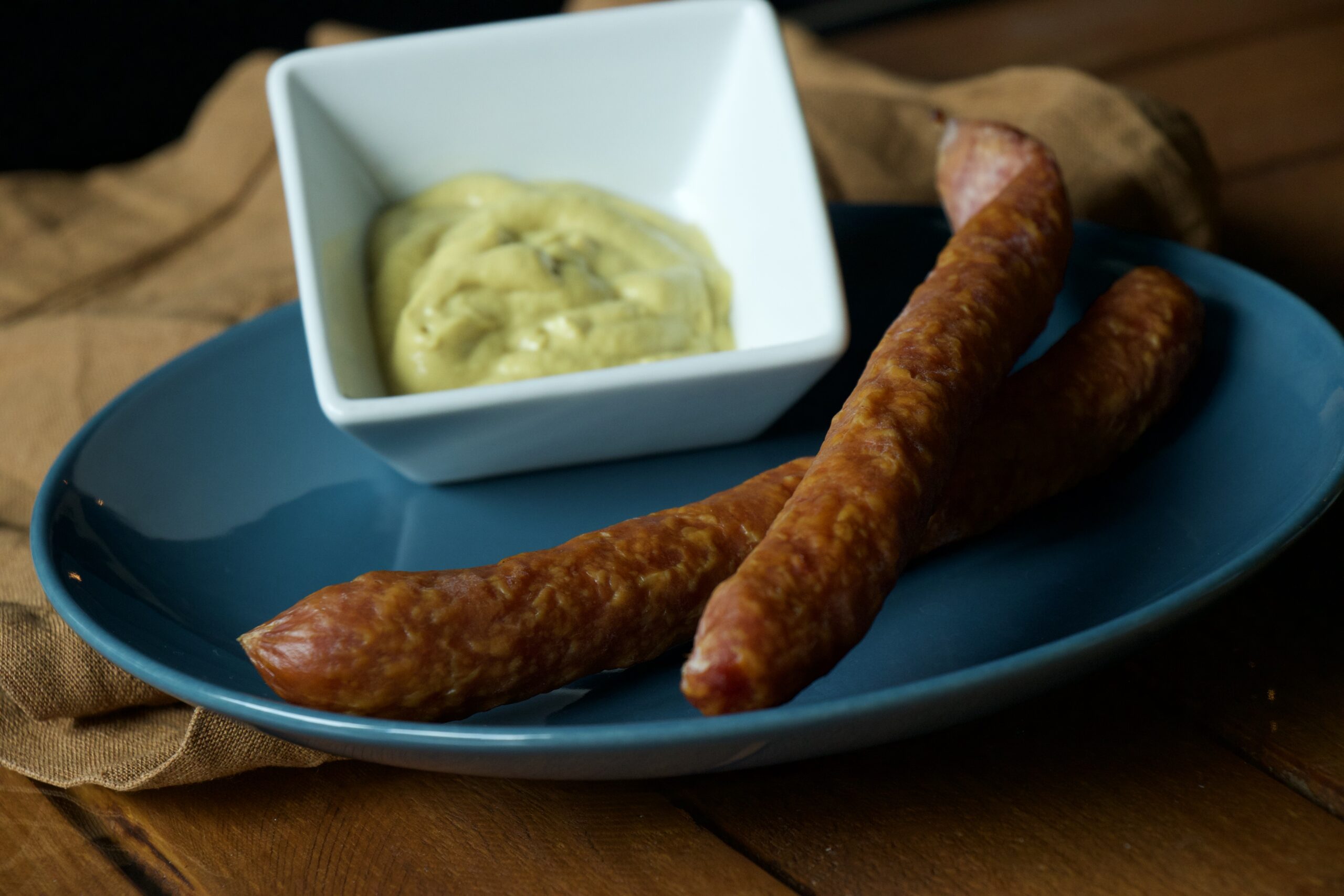 zwei Pfefferbeißer auf einem blauen Teller, daneben eine Schale mit Senf